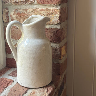White ceramic pitcher on a brick surface with a neutral wall in the background