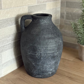 Black vase on a wooden surface with a tiled wall background