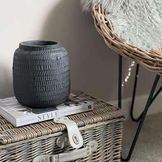 Black textured vase on a stack of books with a wicker basket and chair in the background