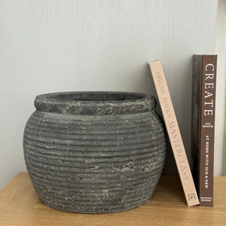 Textured gray pot on a wooden surface with two books in the background.