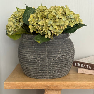 Decorative stone vase with green flowers on a wooden table against a white wall.