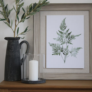 Decorative setup with a black vase, white candle, and framed botanical print on a wooden surface.