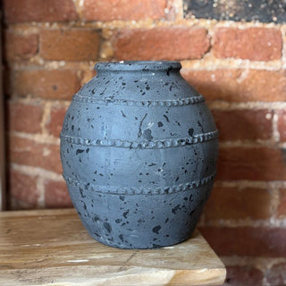 Decorative black speckled vase on a wooden surface with a brick wall background