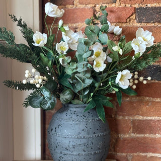 Gray textured vase with a bouquet of white flowers and greenery against a brick wall.