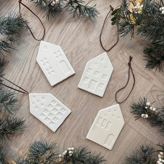 White ceramic house-shaped ornaments on a wooden surface with Christmas decorations.