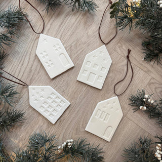 White ceramic house-shaped ornaments on a wooden surface with Christmas decorations.