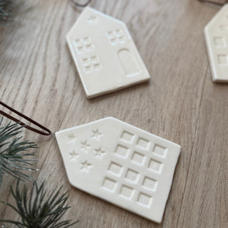 White ceramic house-shaped ornaments on a wooden surface with Christmas tree branches.