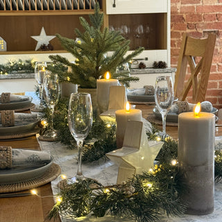 Decorated Christmas table with candles, glasses, and greenery in a cozy indoor setting.