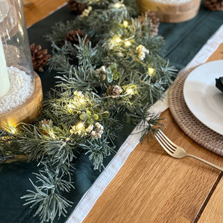 Decorative table setting with greenery, candles, and cutlery on a wooden table.