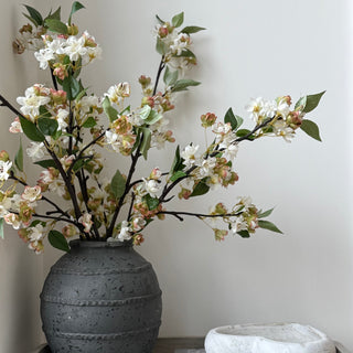 Decorative vase with artificial flowers on a shelf against a plain wall