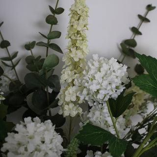 A faux flower arrangement featuring a bundle of white and green flowers with textured foliage.