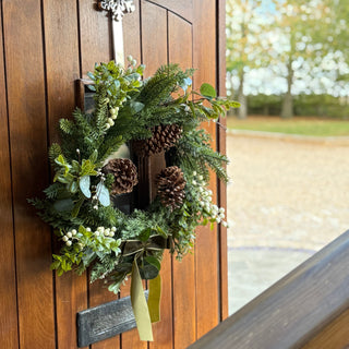 Christmas wreath with pine cones and berry detail on a wooden door.