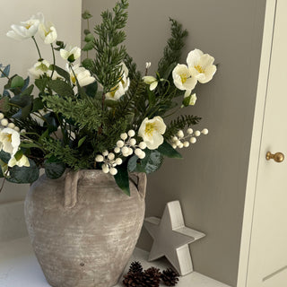 Decorative arrangement of flowers in a textured vase on a shelf with a neutral background