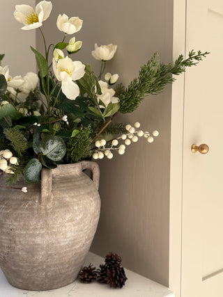 Decorative vase Fir branch, white flowers and Winter berry  arrangement  on a surface against a neutral wall.