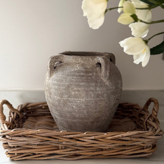 Gray terracotta vase on a wicker tray with white flowers against a light background