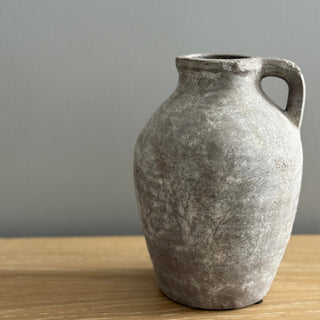 Gray textured stone jug vase on a wooden surface with a gray background