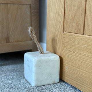 White marble door stopper with a rope handle on a carpeted floor next to wooden furniture.