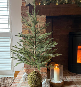 Decorative indoor scene with a small Christmas tree, candle, and star against a brick wall.