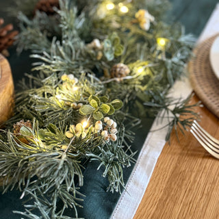 Decorative table setting with a green garland, lights, and wooden elements on a table.