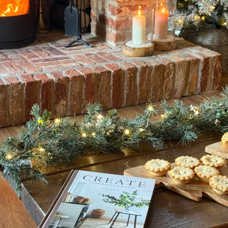 Decorative fireplace with garland, candles, and a book titled 'Create' in a cozy setting.