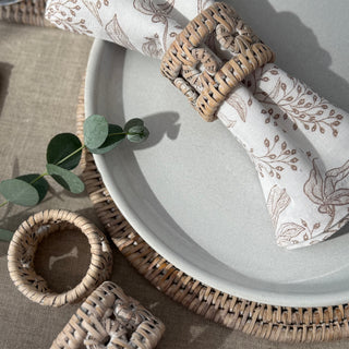 Decorative table setting with woven napkin rings and patterned napkins on a textured surface.