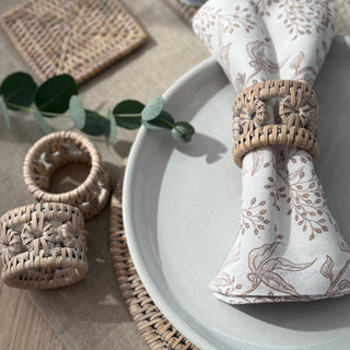 Table setting with a patterned napkin, woven napkin ring, and decorative elements on a wooden surface.