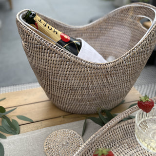 Woven rattan wine cooler basket with a bottle of Moet champagne on a wooden table outdoors.