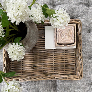 Wicker tray with a small box on a textured surface with white flowers.