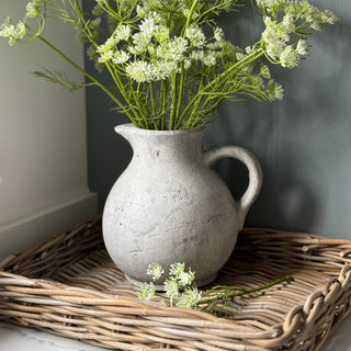 Grey pitcher with greenery on a woven tray against a gray wall