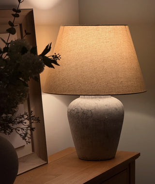 Table lamp with textured base and beige shade on a wooden surface.