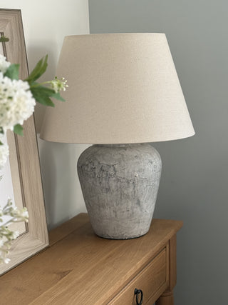 Table lamp with a stone textured base and beige shade on a wooden surface against a gray wall.