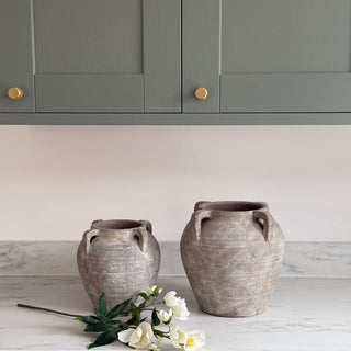 Two gray ceramic vases on a white countertop with gray cabinets in the background.
