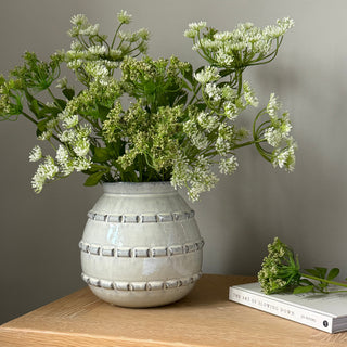 Decorative vase with greenery on a wooden shelf against a neutral wall.