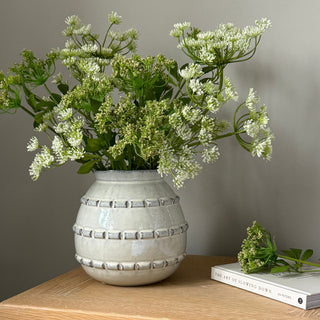 Decorative vase with greenery on a wooden shelf against a neutral wall.