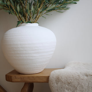 White ceramic vase with faux olive branch on oak bench