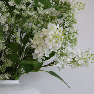 Arrangement of white flowers and green leaves against a plain background