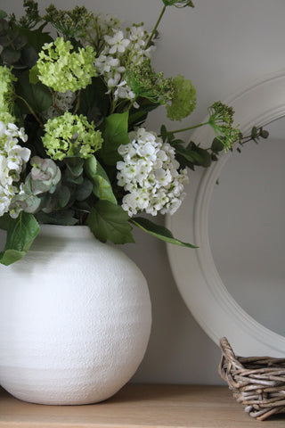 A white ceramic vase with a round shape and a textured surface with a floral display.