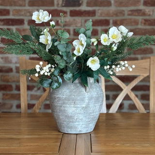 Faux floral arrangement in a textured vase on a wooden table with a brick wall background