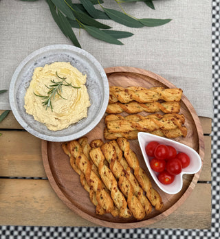 Platter with hummus, breadsticks, and cherry tomatoes on a wooden and marble board.
