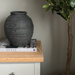 speckled black vase on bedside table next to olive tree