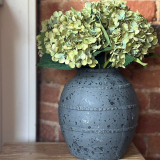 Decorative vase with green flowers against a brick wall