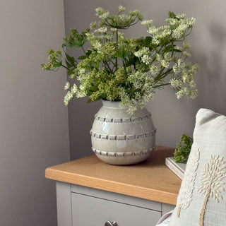 Decorative arrangement with flowers and a textured vase on a shelf against a neutral wall.