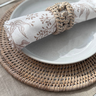 Decorative napkin with a floral pattern on a white plate, placed on a woven placemat.