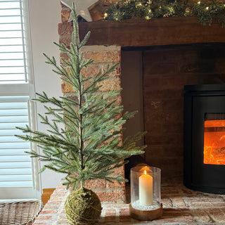 faux fir Christmas tree on brick fire place next to candle 