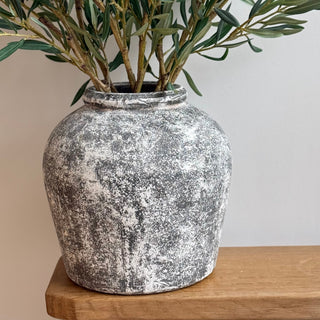 Decorative vase with olive branch on a wooden surface against a neutral background