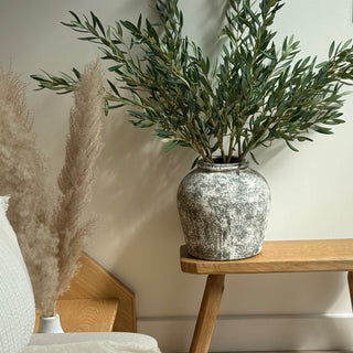 Decorative vase with greenery on a wooden side table in a room setting.