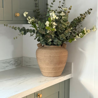 Vase with greenery on a kitchen counter with cabinets and marble backsplash.