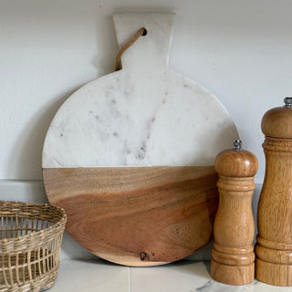 Marble and wooden cutting board with a wicker basket and wooden salt and pepper shakers on a marble surface.