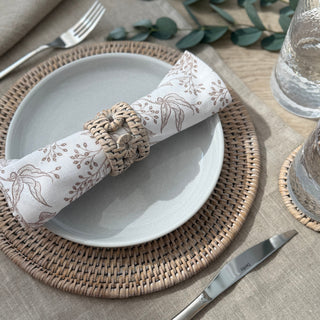 Dining table setting with a woven placemat, white plate, silver knife, and floral napkin.