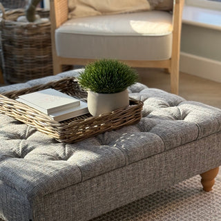 Gray upholstered bench with a woven tray holding books and a plant, in a home setting.